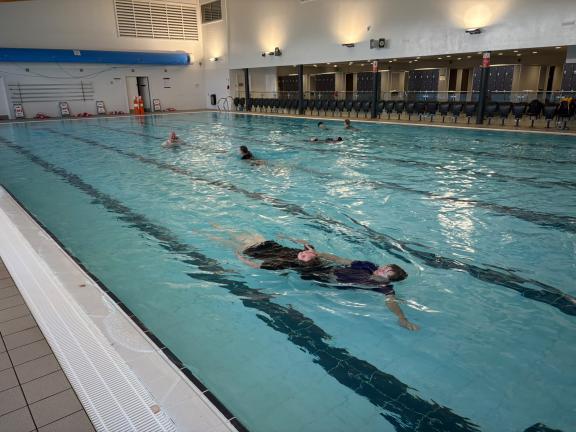 In swimming pool practicing saving someone swimming with them backwards